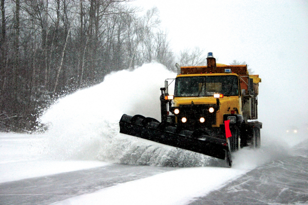 A snow plow truck plowing snow off the road.