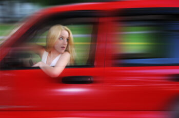 Woman driving a red car blurred because she is speeding.