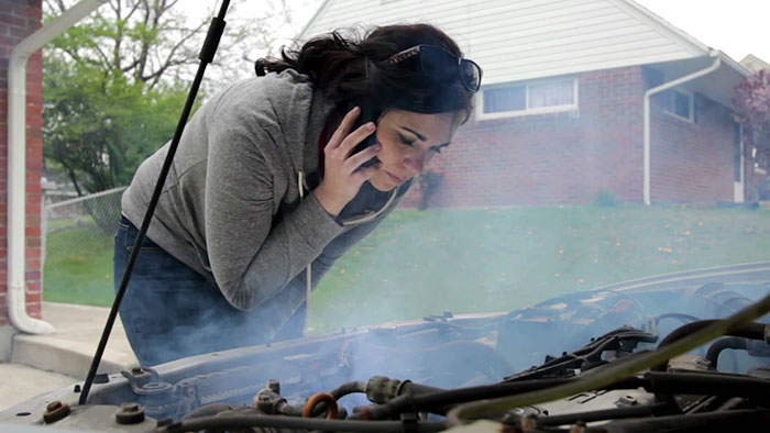 Woman on a phone trying to diagnose her car that is smoking from the hood.