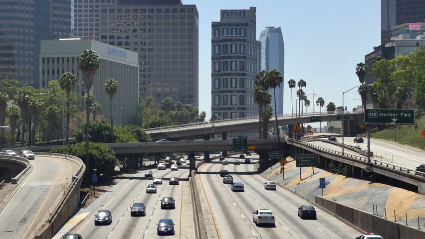 Image of an interstate with a bunch of cars driving on it with buildings in the background.