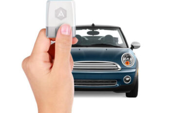 A hand holding a remote key pointed at a car.