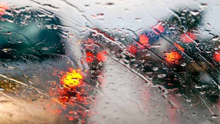 Up close image of rain on a window with traffic behind it.