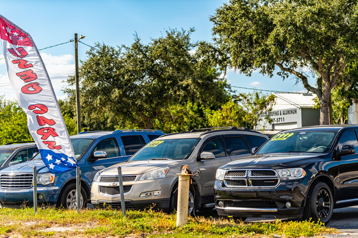 Local used car auto dealer dealership with cars parked on parking lot display with price tags on windshield windows in Florida small town city