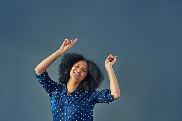 A happy young woman does a very happy dance against a gray background