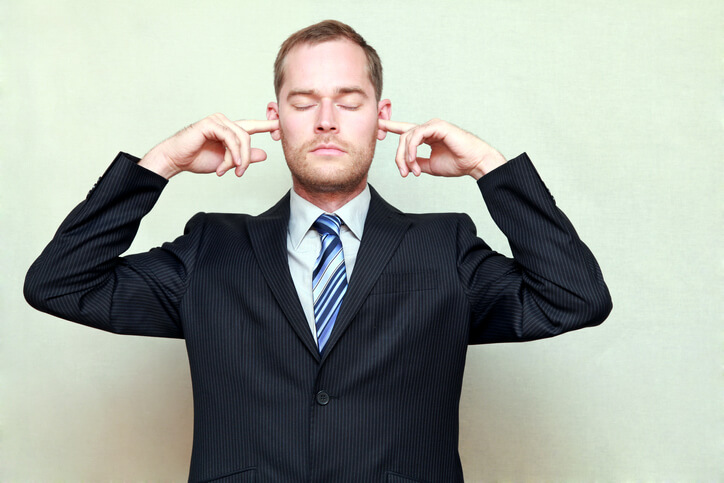 Portrait of young handsome businessman with closed eyes and fingers in ears, not listening, isolated on gray