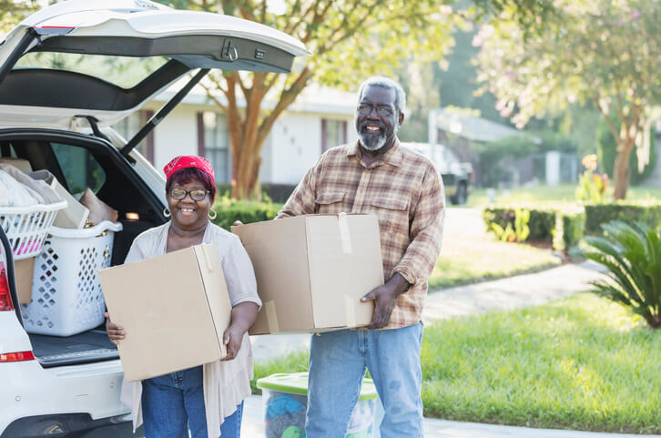 A senior African-American couple relocating, moving to a new home in Florida. They are excited, unloading boxes from their car