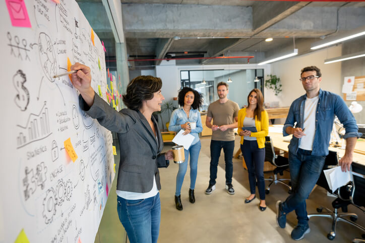 Latin American woman making a business presentation in a meeting at a creative office and pointing to her team her business plan