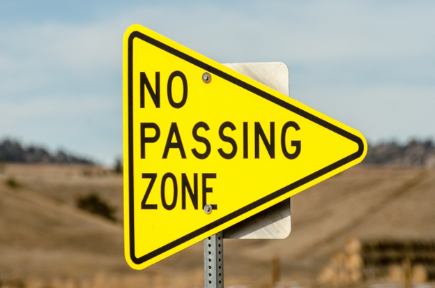 A pennant-shaped road sign indicates a no passing zone next to a United States highway.