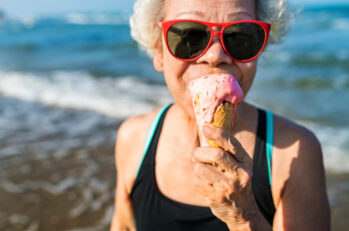 Senior woman eating an ice-cream after driving to the beach.
