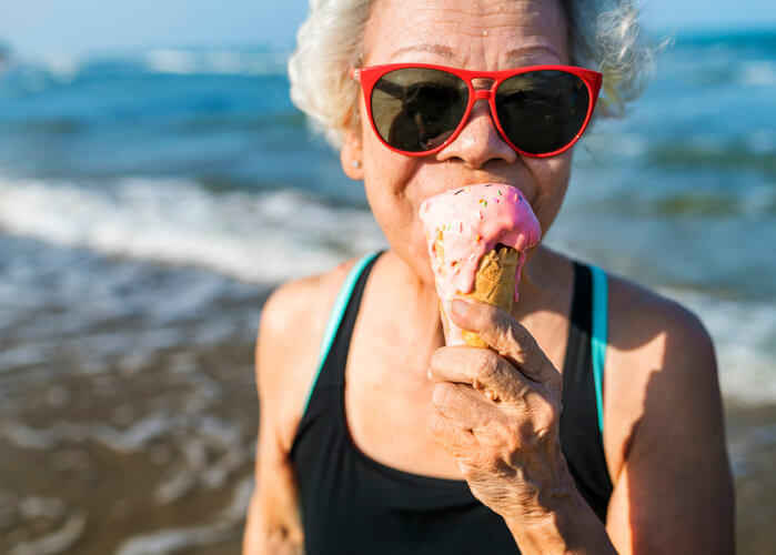 Senior woman eating an ice-cream after driving to the beach.