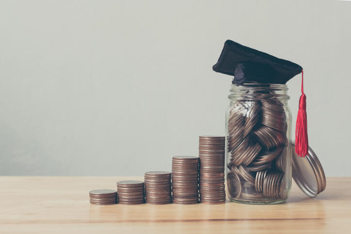 Increasingly tall stacks of quarters lead to a mason jar full of them topped with a graduation cap.