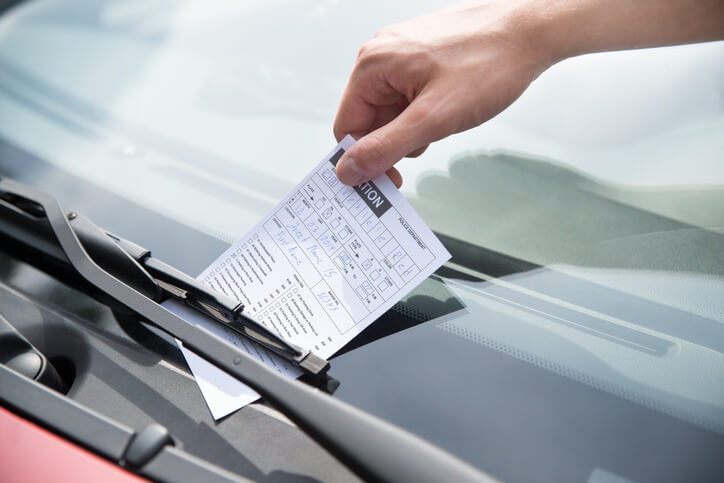 A person retrieving a New Mexico traffic ticket off of their windshield.